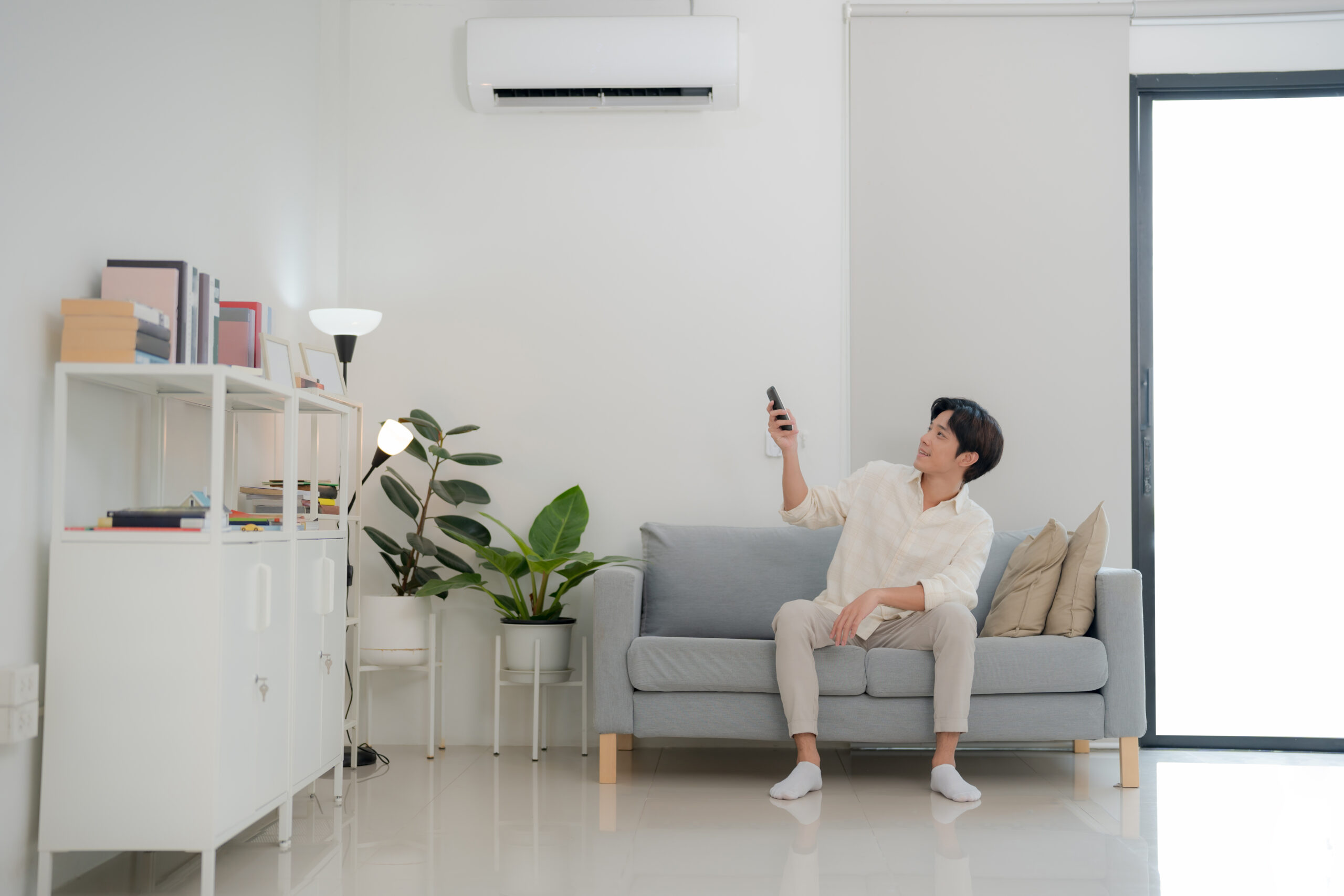 Man sitting on sofa using remote to control air conditioner